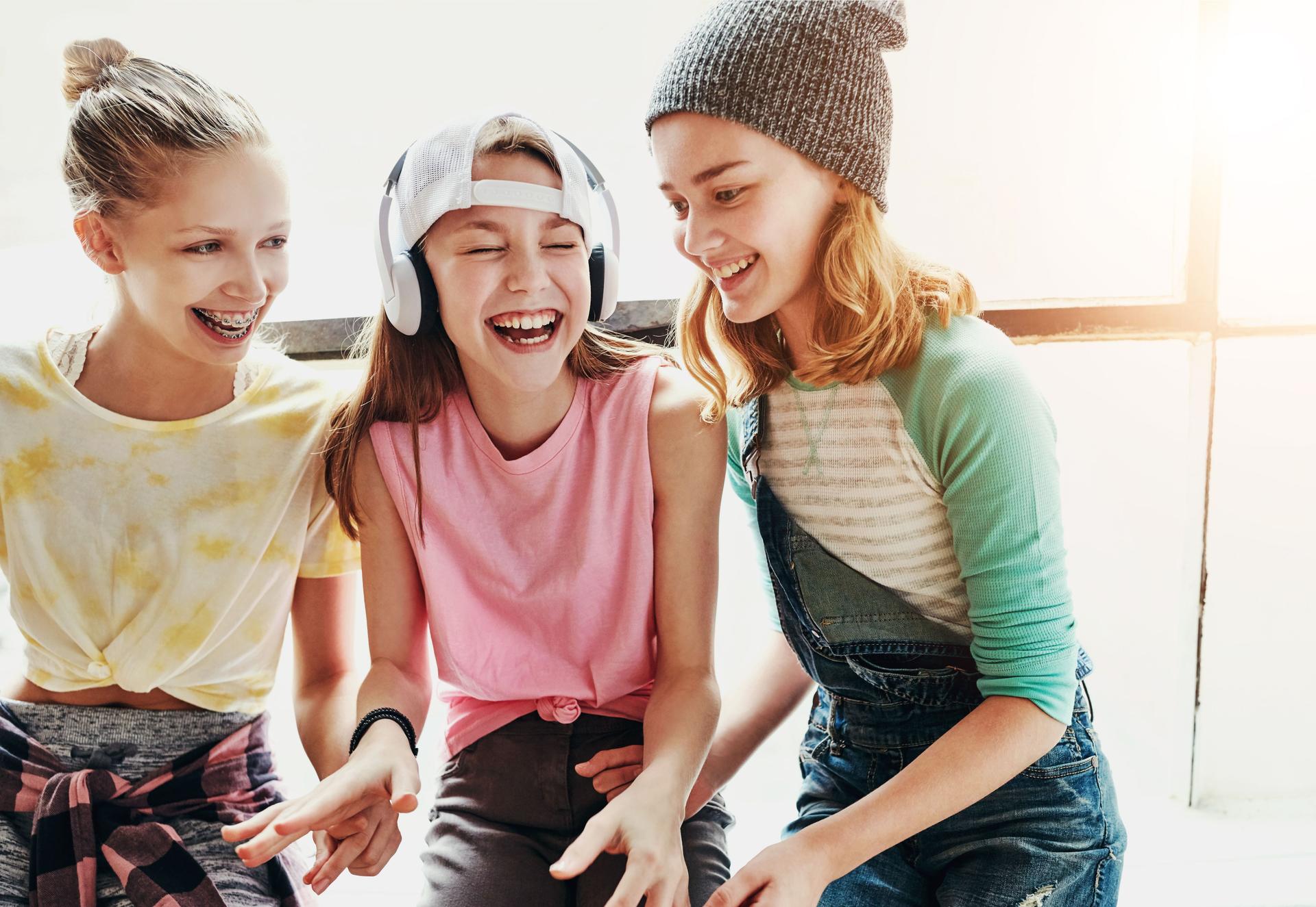 Girl, teen group and friends with headphones for music, streaming kpop playlist and bonding together inside. Youth, happy and female people with listening to audio, edm sound track and fun weekend