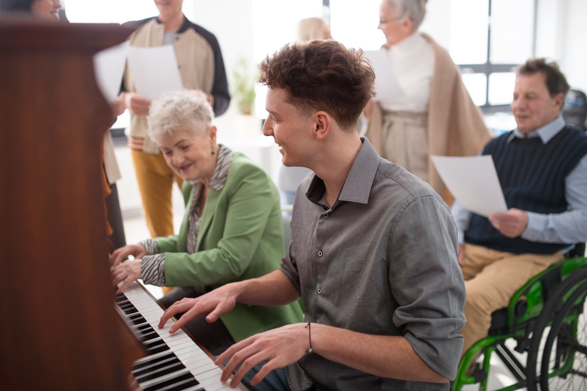 Senior woman with young teacher playing at piano in choir rehearsal.
