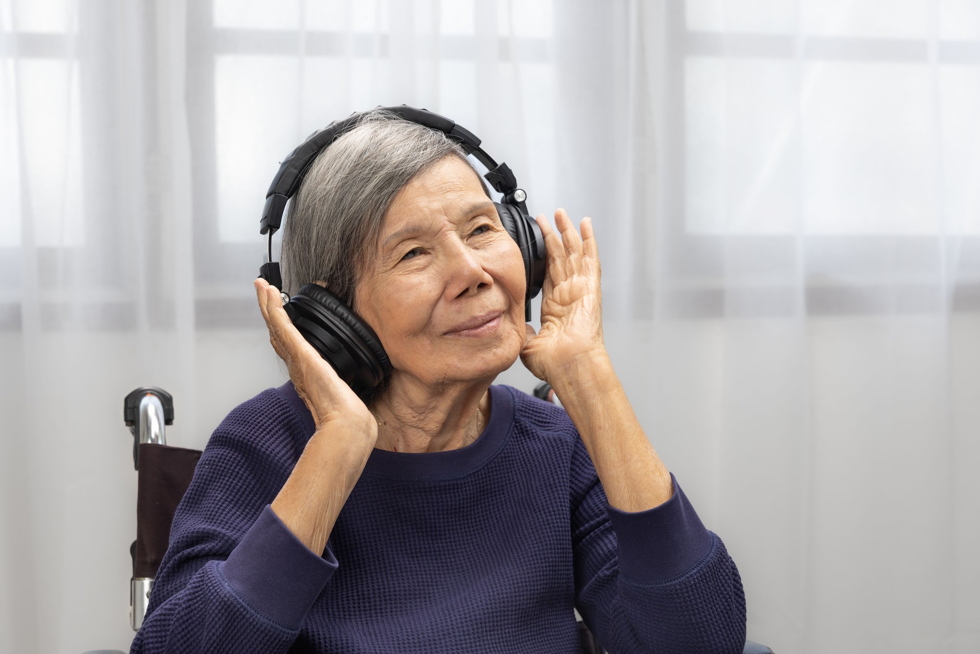 Asian senior woman listening music with headphone at home